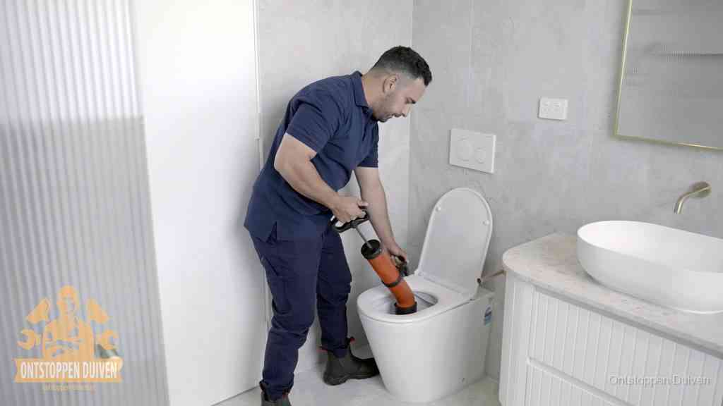 Een monteur buigt over een wandcloset en duwt met de hand een persluchtontstopper in de toiletpot om de verstopping handmatig los te maken in Duiven