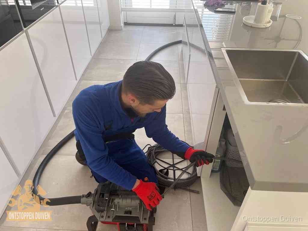 Een monteur ontstopt de keukenafvoer onder de spoelbak met een elektrische veermachine in Duiven Een monteur ontstopt de keukenafvoer onder de spoelbak met een elektrische veermachine in Duiven