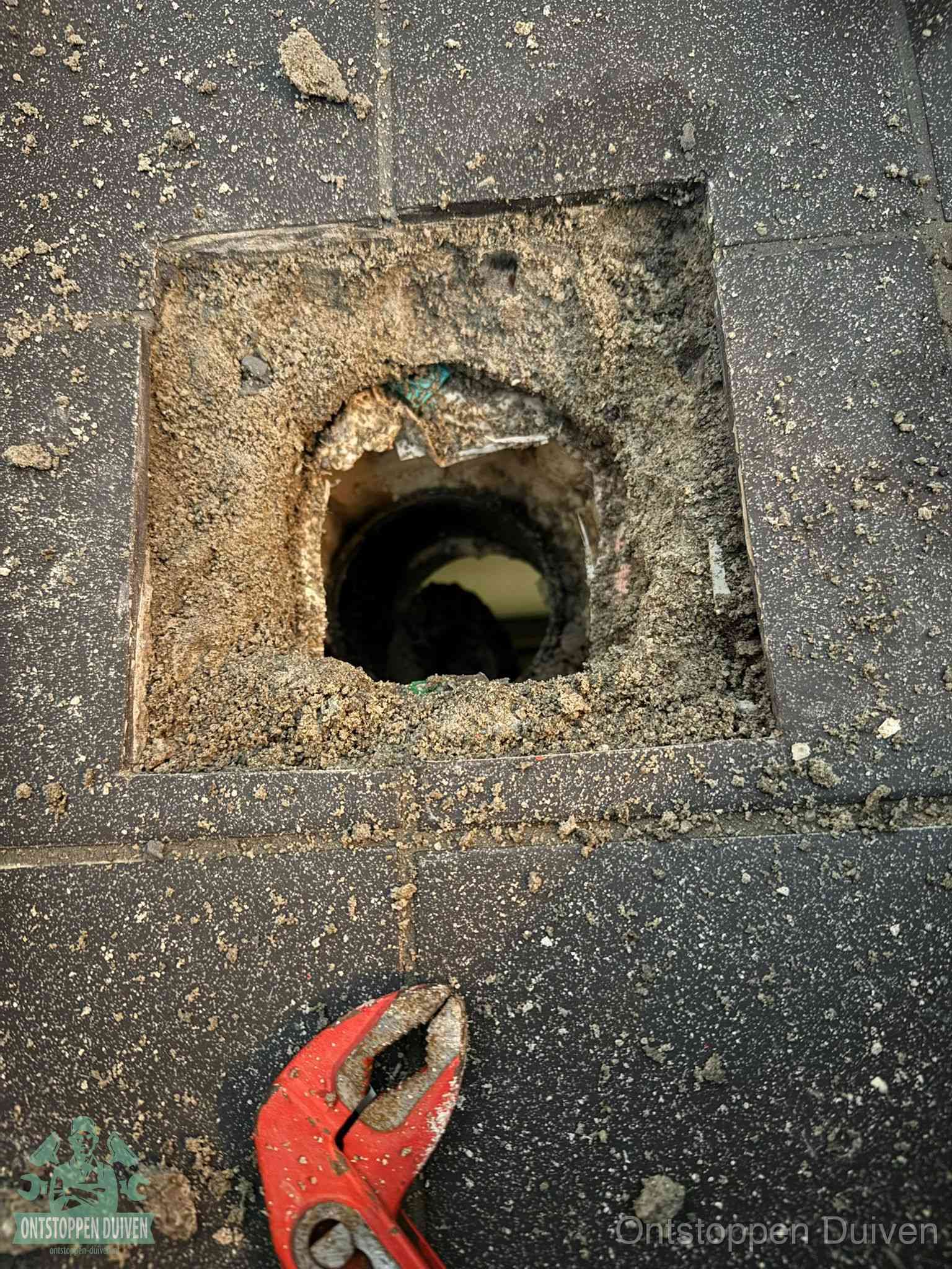 Een geopend rioolputje in een betontegelvloer met losgemaakt rooster en een zichtbare ronde afvoerbuis, het achterhalen waar de afvoerverstopping zit in Duiven