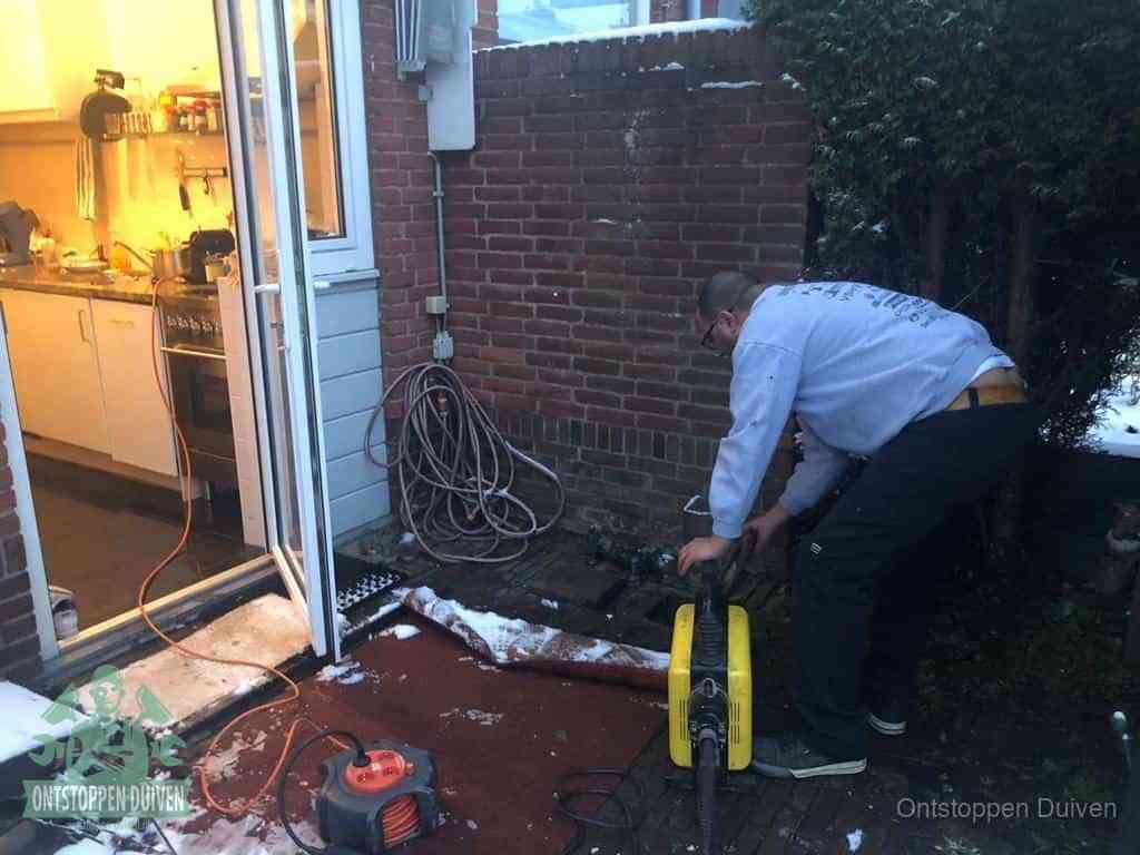 Een monteur werkt buiten bij een open riool-/grondput met een elektrische ontstoppingsmachine om een verborgen afvoerprobleem op te sporen in Duiven