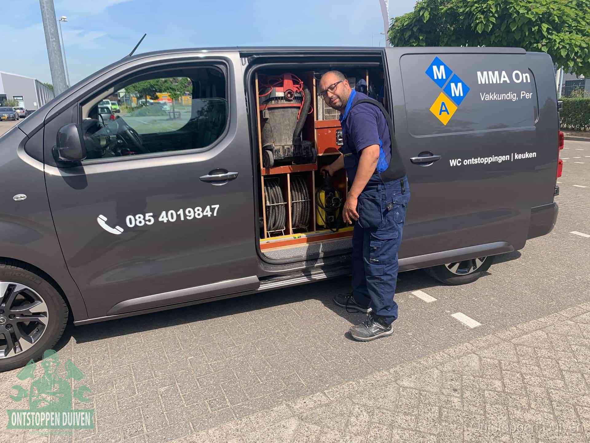 Een monteur bij de open schuifdeur van zijn bedrijfsbus op een parkeerplaats, klaar om de oorzaak van terugkerende afvoerverstoppingen aan te pakken in Duiven