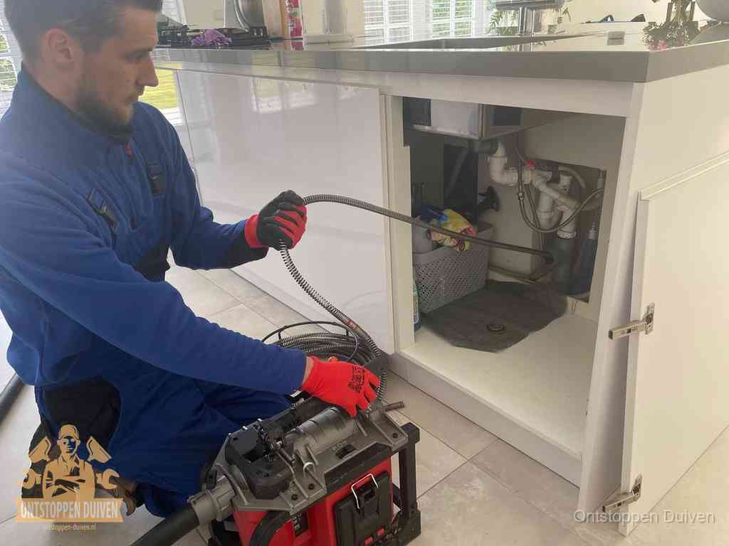 Een monteur reinigt de keukenafvoer grondig met een veermachine om terugkerende gootsteenverstoppingen te voorkomen in Duiven Een monteur reinigt de keukenafvoer grondig met een veermachine om terugkerende gootsteenverstoppingen te voorkomen in Duiven