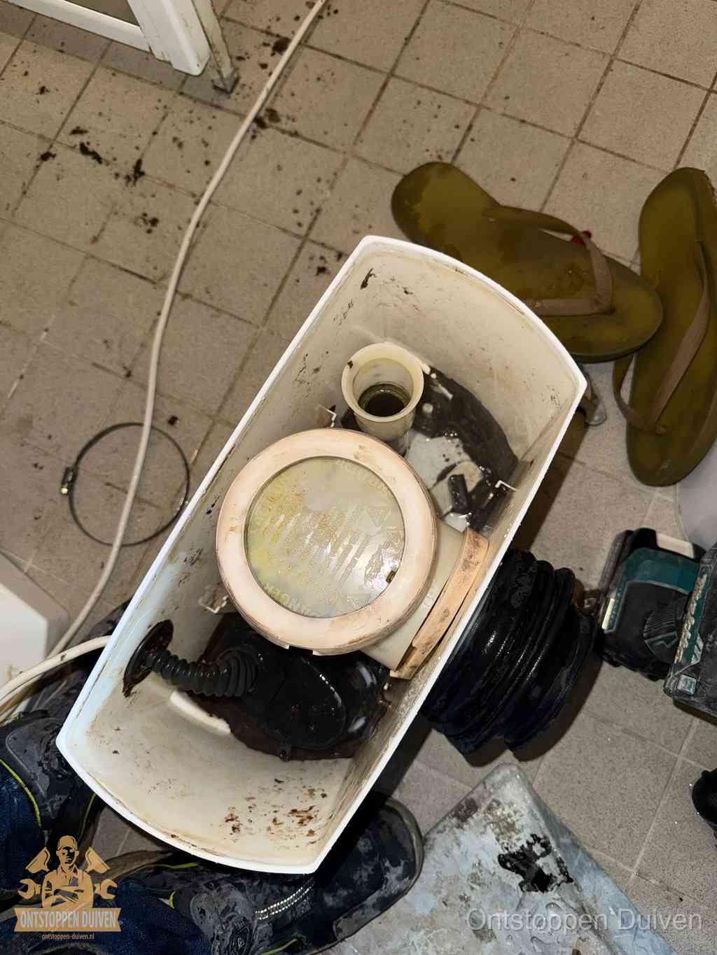 Een gedemonteerde toiletpot op de vloer met ontstoppingsveer en gereedschap ernaast, het verwijderen van een vastzittend voorwerp uit de wc in Duiven