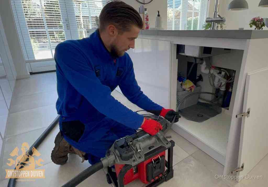 Een monteur voert een professionele elektrische ontstoppingsmachine in de afvoer onder de spoelbak tijdens het gootsteen ontstoppen in Duiven Een monteur voert een professionele elektrische ontstoppingsmachine in de afvoer onder de spoelbak tijdens het gootsteen ontstoppen in Duiven