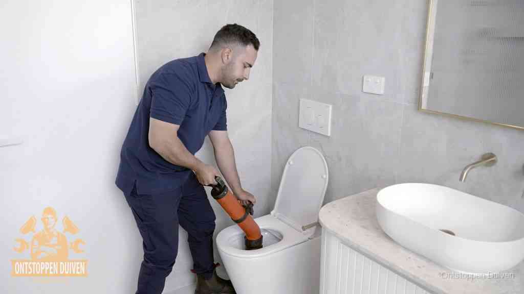 Een man gebruikt een handmatige luchtdruk-ontstopper in een modern betegeld toilet om zelf de wc te ontstoppen in Duiven